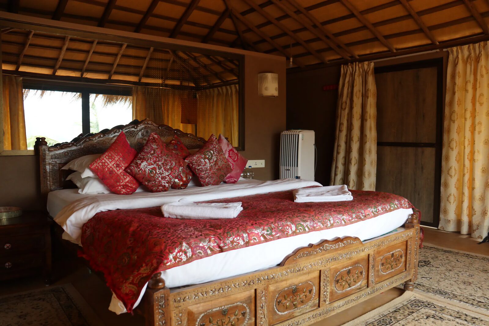A hand-carved bed with red silk bedding beneath the thatched roof