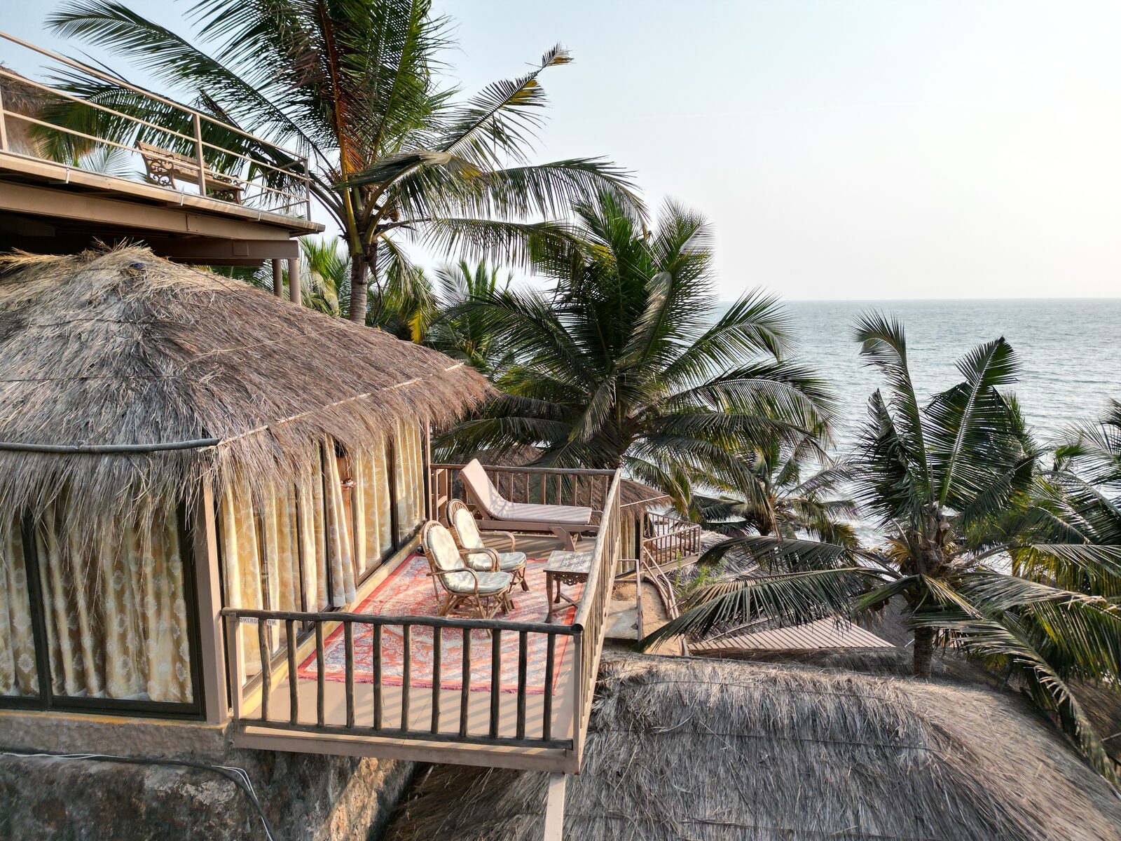 A thatched cottage and its balcony among the coconut palms, the sea beyond